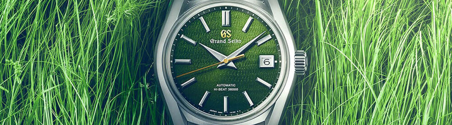Grand Seiko SBGH351G with a textured green dial, silver hour markers, and gold seconds hand set against vibrant green grass blades